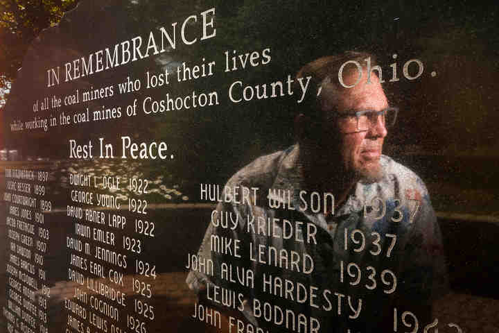 Sam Bennett is reflected in a Coal Miners Memorial Saturday, July 28, 2018, in Coshocton, Ohio. Mr. Bennett raised $60,000 to have the memorial installed on the lawn of Coshocton County Courthouse in 2013.  (Jeremy Wadsworth / The Blade)